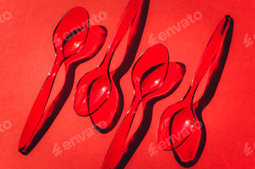 Preview: Disposable plastic spoons on red background with contrasting shadows.