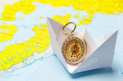 Preview: Paper boat with compass sailing on a colorful world map