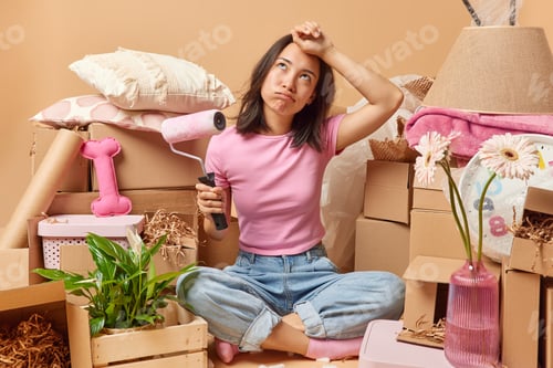 Preview: Tired Assian woman wipes sweat on forehead feels tired to paint walls in new apartment sits crossed