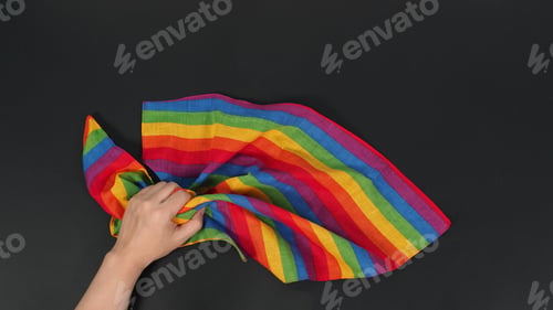 Preview: Hand is holding rainbow handkerchief on black background.