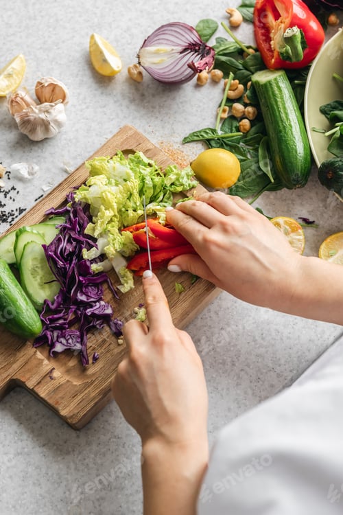 Preview: A woman cuts a fresh bell pepper on a wooden board in the kitchen.