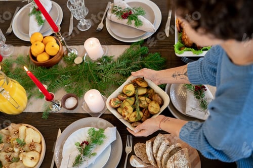 Preview: Hands of young housewife putting homemade baked potatoes on festive table