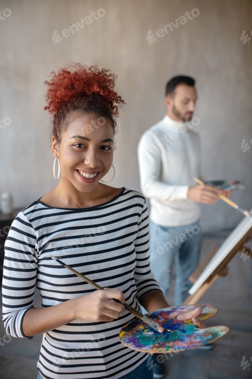Preview: Appealing artist wearing striped shirt mixing gouache