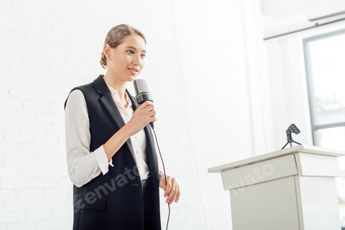 Preview: attractive businesswoman holding microphone and talking during conference in conference hall