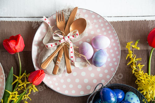 Preview: Close up of plate with cutlery, easter eggs and flowers top view.