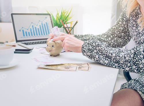 Preview: businesswoman in a gray dress holds a piggy bank in her hands while sitting on a chair