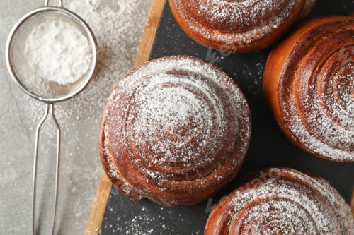 Preview: Board with cinnamon rolls with powdered sugar on grey background, top view