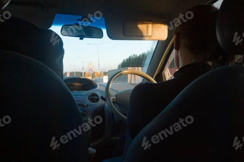 Preview: a young woman sits behind the wheel and looks at the phone in her hand
