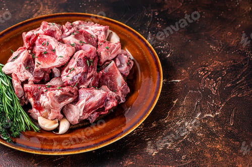 Preview: Raw mutton meat diced for goulash or stew with bone on a rustic plate. Dark background.