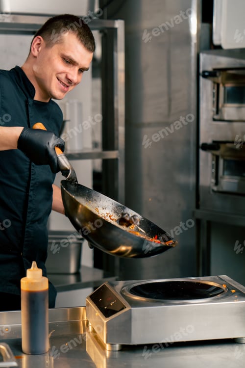 Preview: chef in the kitchen holding a frying pan with noodles and smiling happy with the result