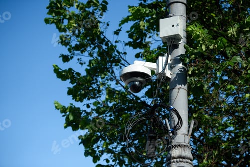 Preview: close up view of security camera on street pole with tree foliage in sunlight