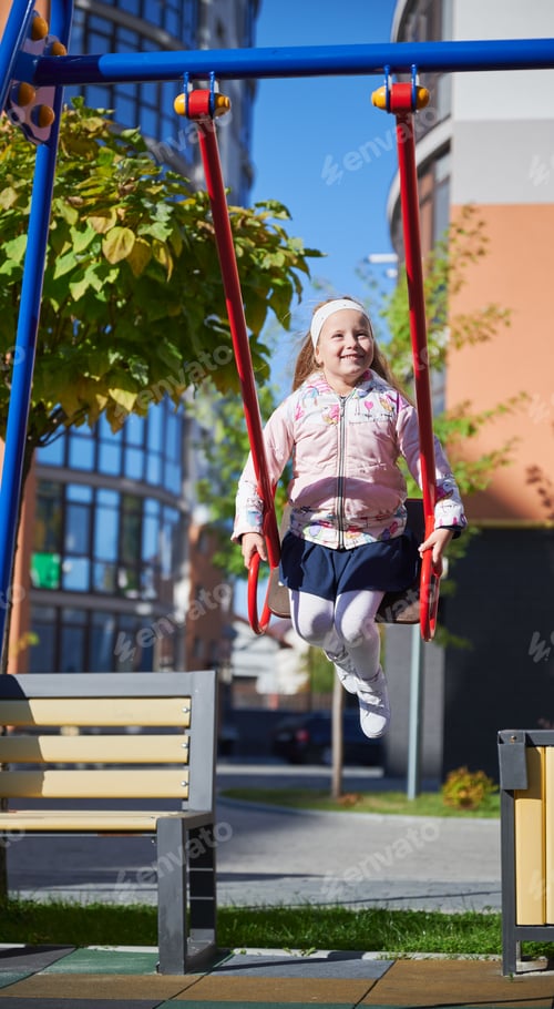 Preview: Little girl swinging on colorful swing at playground.