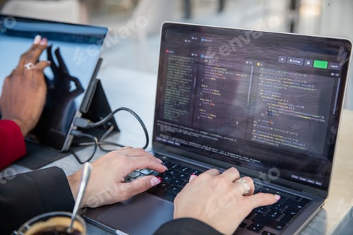 Preview: Female programmer writes some code and drinks coffee while sitting near her colleague.