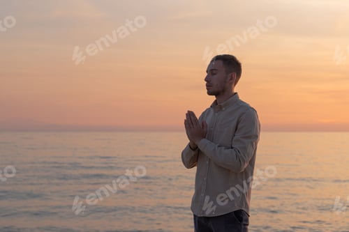 Vista previa: joven con camisa, haciendo una oración en una puesta de sol en la playa