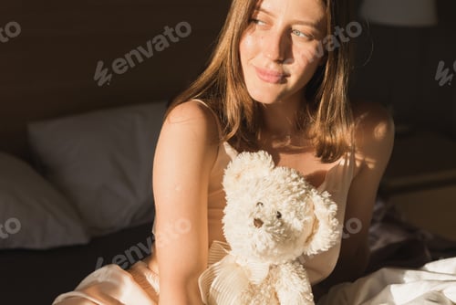 Preview: Portrait woman waking up in her bed, she is smiling and stretching with toy bear. Happy young woman