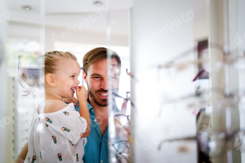 Preview: Health care, eyesight and vision concept. Little girl choosing glasses with father at optics store
