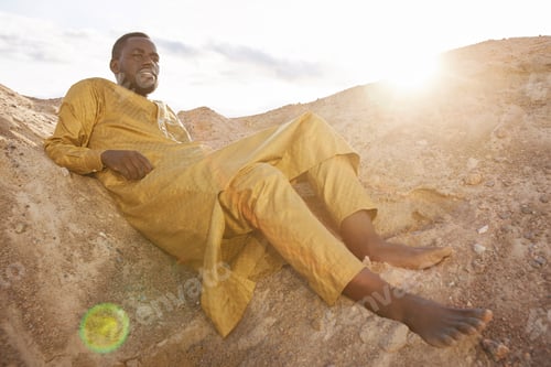 Preview: African American Man in Traditional Kaftan Lying on Sand Dunes in Sunlight