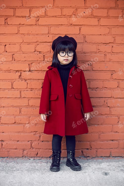 Preview: Korean girl in a red coat and cap and round glasses stands on the iron staircase the street in autum