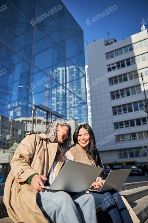 Preview: Cheerful women with laptops sitting on street steps