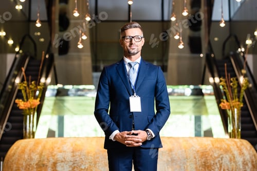 Preview: handsome businessman in suit and glasses with badge in hotel