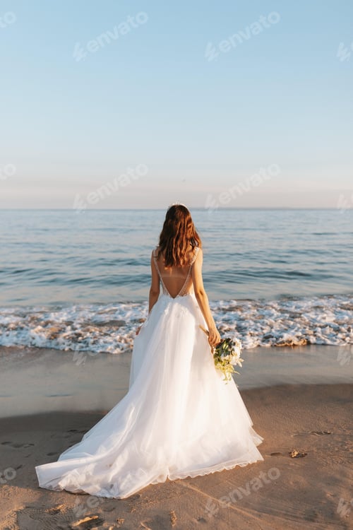 Preview: Bride at the beach looking at ocean waves from behind