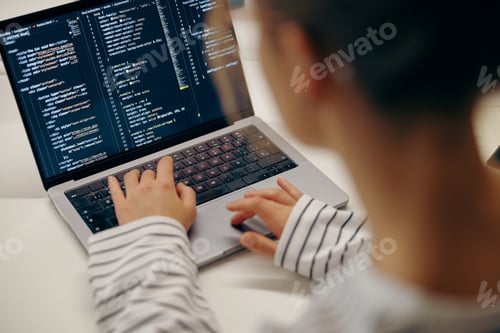 Preview: Close up of female software engineer writing code on laptop with screens setup in coworking