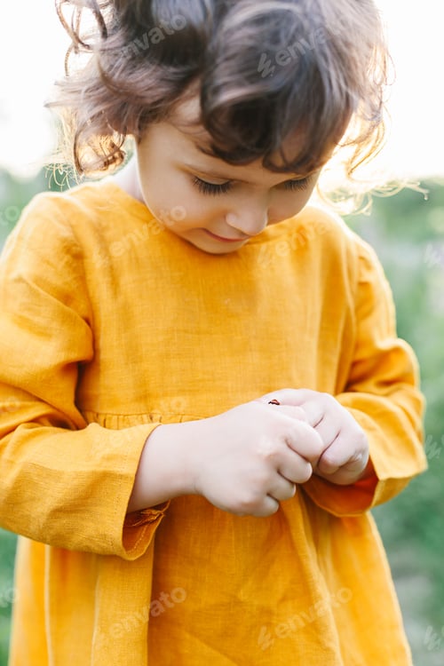 Preview: Adorable little girl wearing mustard linen dress with ladybug among lupine flowers
