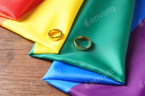 Preview: Wedding rings and rainbow flag on wooden table. Gay marriage