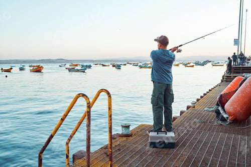Preview: Fisherman casting fishing rod from pier with colorful boats in background in Tongoy, Coquimbo region
