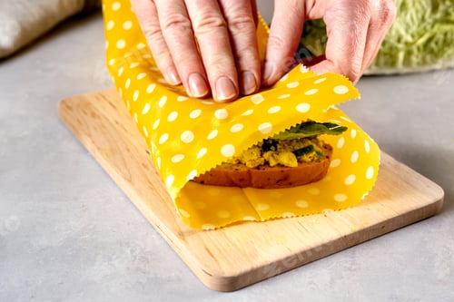 Preview: Woman hands wrapping a healthy sandwich in beeswax food wrap and cotton bag
