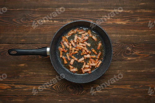 Preview: Cooking crispy bacon in a frying pan on a rustic wooden table