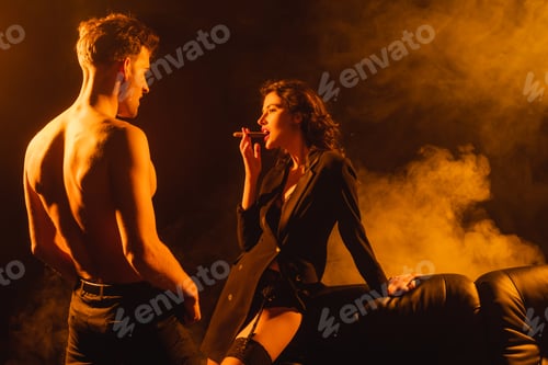 Preview: seductive woman smoking cigar near shirtless man on black