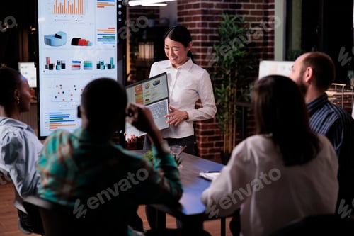 Preview: Smiling asian entrepreneur standing in business office presenting turnover charts on laptop screen