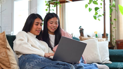 Vorschau: Asiatische Freundinnen benutzen Laptop zusammen auf dem Sofa