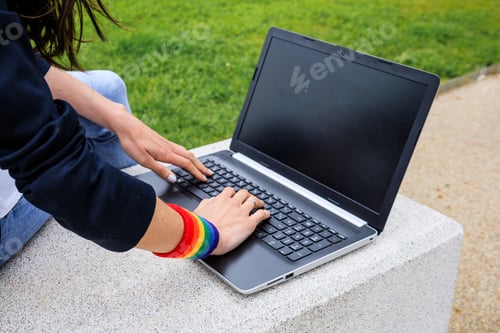 Preview: Close-up of woman hands with laptop and LGBT bracelet in modern park . LGBTQIA culture.