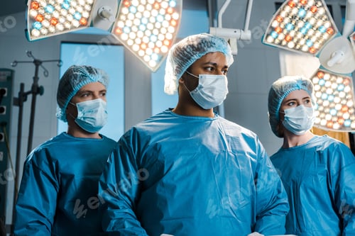 Preview: doctors and nurse in uniforms and medical masks looking away in operating room