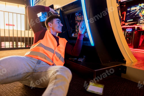 Preview: echnician wearing a safety vest while repairing an arcade machine in a vibrant gaming center.