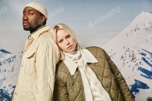 Preview: young interracial couple in warm clothes with mountain background looking at camera, winter concept