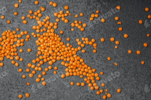 Preview: Bright orange beads scattered on a textured gray surface in natural light