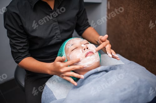 Preview: Young beautiful girl in mask for face relaxing in spa salon.