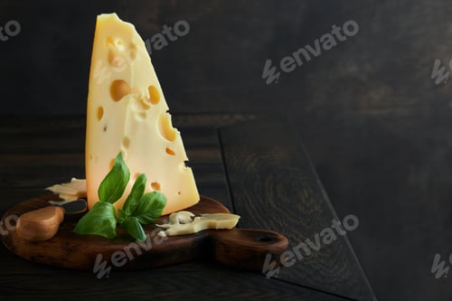 Vista previa: Cheese. Piece of cheese triangle, Swiss cheese on with basil and a knife on a serving board on dark
