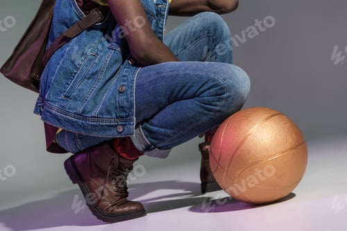 Preview: cropped shot of african american man crouching with golden basketball ball on grey