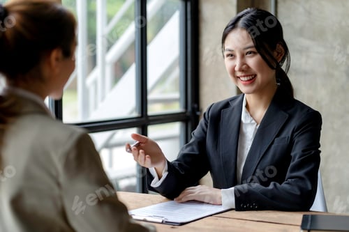 Preview: Smiling young Asian businesswomen talking to colleague and exchanging ideas together at office.