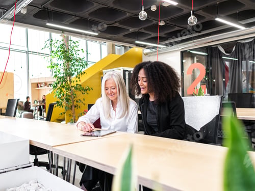 Preview: Cheerful diverse colleagues using tablet in modern workspace