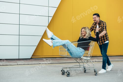Preview: Couple riding in a shopping cart while outside of the supermarket or mall