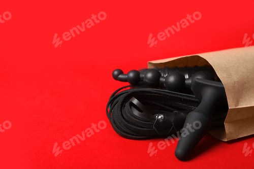 Preview: Paper shopping bag with different sex toys on red background. Space for text