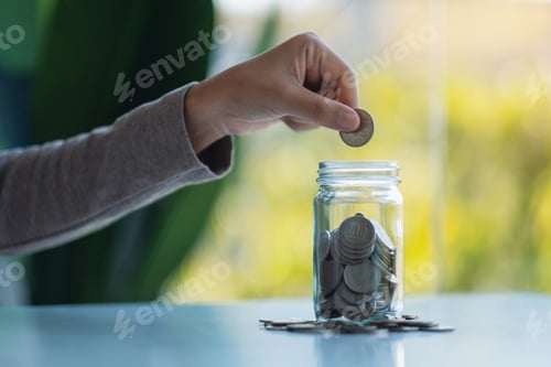 Preview: Hand Placing Coin into Glass Jar for Savings