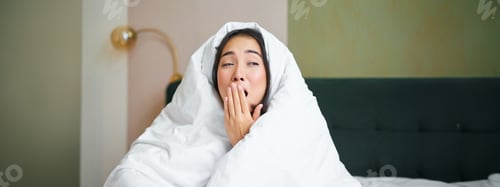 Preview: Close up of funny sleepy girl, asian woman yawns after waking up early morning, covers herself with