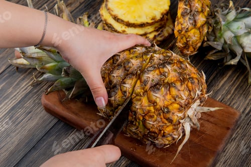 Preview: side view of woman hands cutting pineapple with knife on cutting board with sliced pineapple