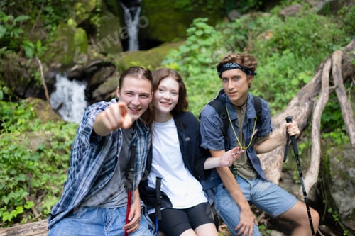 Preview: Group of friends with backpacks and sticks sitting on a fallen tree, Take a break during the hike